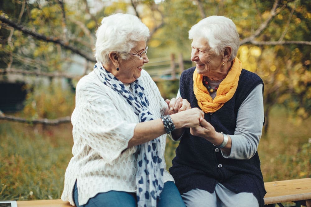 female senior living residents outside clasping hands